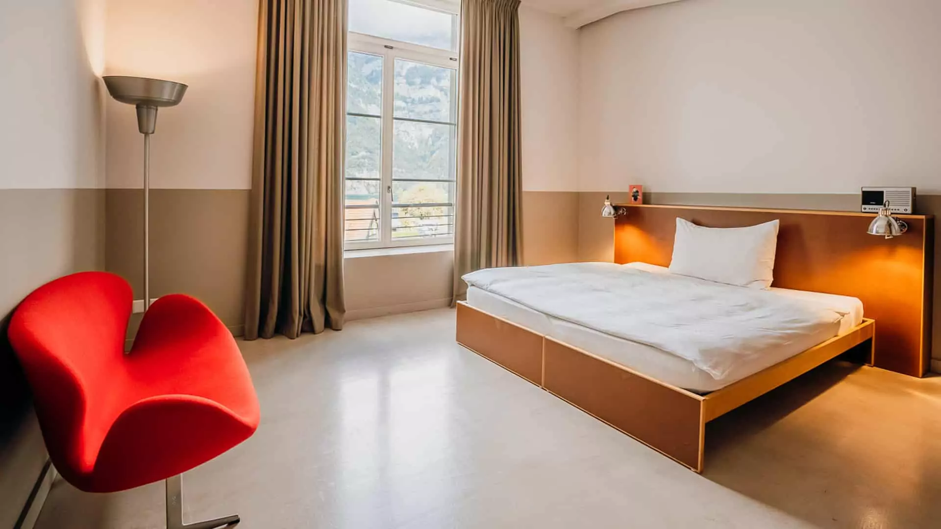 Geräumiges Loftzimmer mit breitem Doppelbett, rotem Sessel und stylischer Designer-Lampe im Lofthotel Murg.
