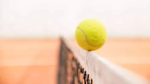 A yellow tennis ball balances on the edge of a net
